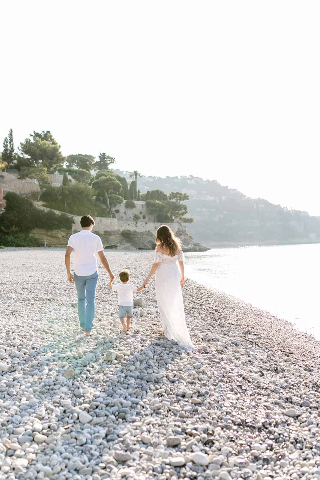Pregnant family outdoor photoshoot. Mum and Dad walk hand in hand with toddler on the beach in Monaco