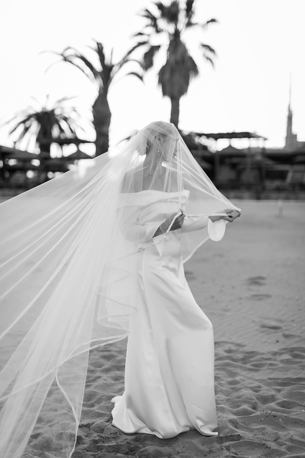 back and white editorial wedding image of bride covered in in veil on aa beach