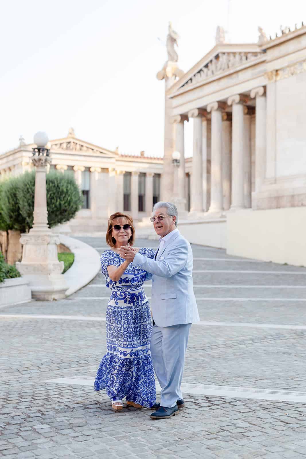 Elegant family photography of grandparents dancing in front of Athens Academy building by Athens family photographer Anette Cook